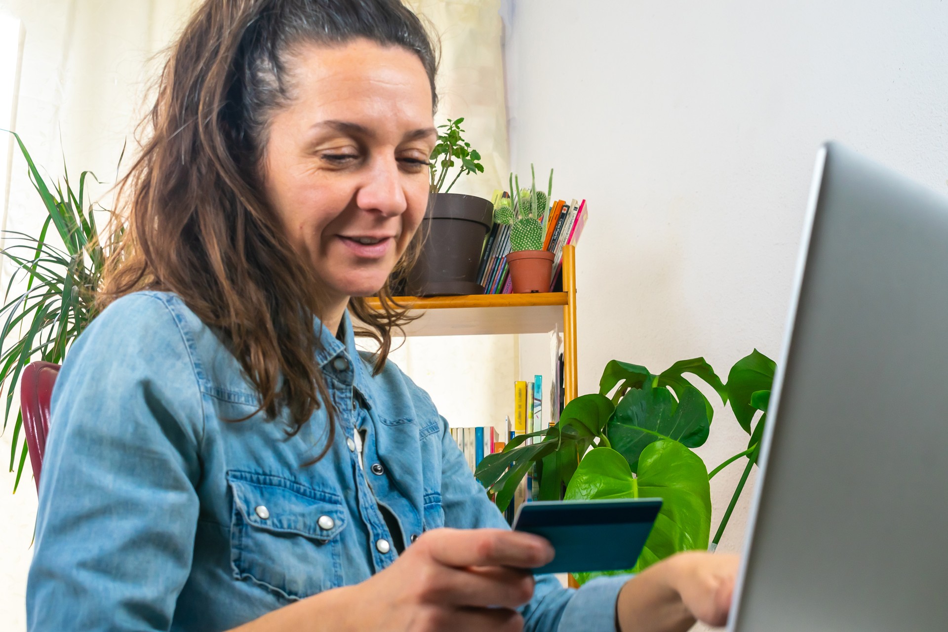 adult woman holds her bank card and smiles looking at her computer financial technology, copy space